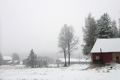 Snö och dimma ger ett landskap i gråskala som konstrateras av röda byggnader